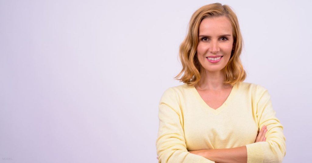 woman (model) with arms crossed on a light purple background smiling